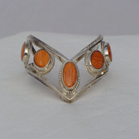 Five fouteen by ten millimeter oval Orange Oyster shell bezel set connected by two triangular wires which are formed to a chevron shape. Worn with chevron pointing down
